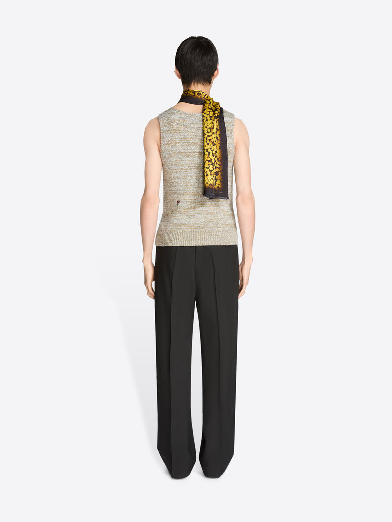 Back view of a person wearing a sleeveless top with a patterned scarf and black pants on a white background