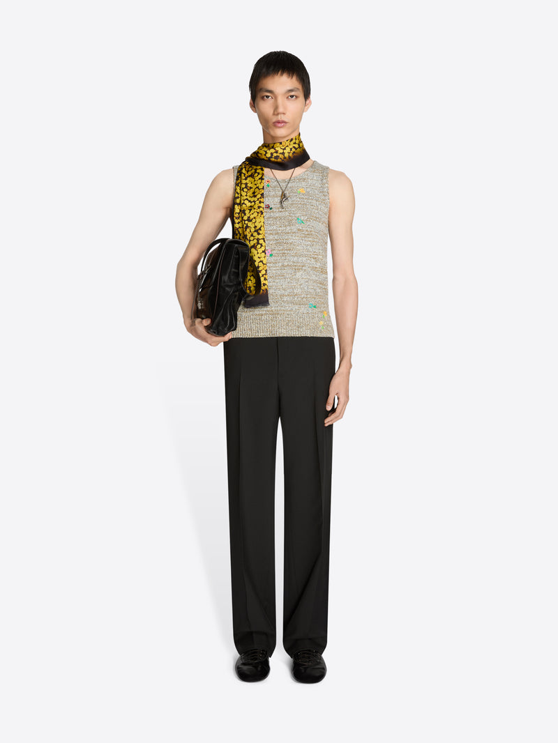 Person wearing a sleeveless top, black pants, scarf and holding a black bag on a white background