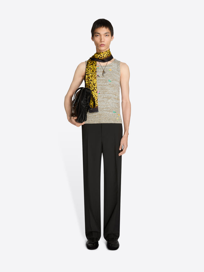 Person wearing a sleeveless top, black pants, scarf and holding a black bag on a white background