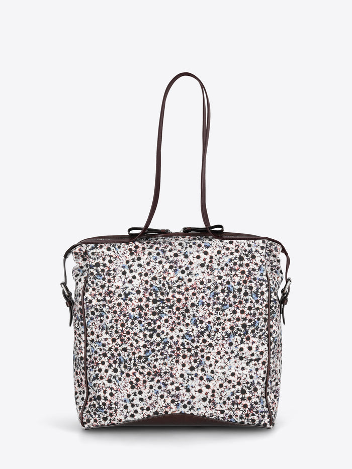 A structured tote bag with a dense multicolor floral print pattern on a white base, featuring dark brown leather trim and shoulder straps.