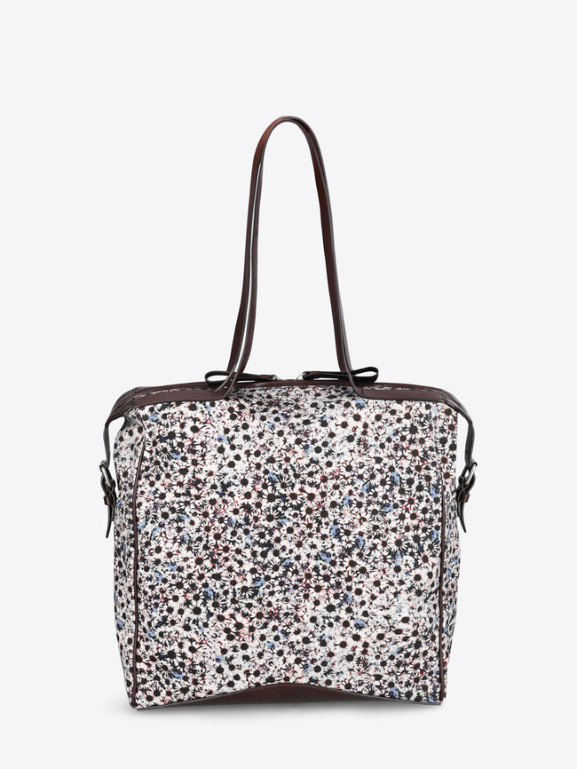 A structured tote bag with a dense multicolor floral print pattern on a white base, featuring dark brown leather trim and shoulder straps.