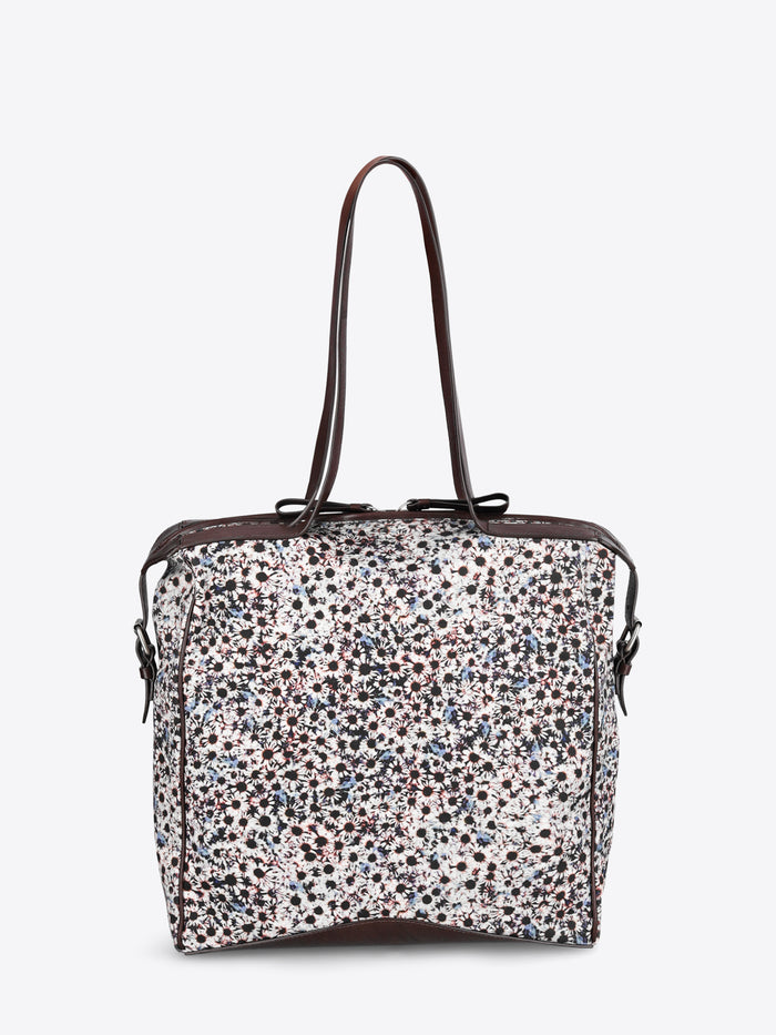 A structured tote bag with a dense multicolor floral print pattern on a white base, featuring dark brown leather trim and shoulder straps.