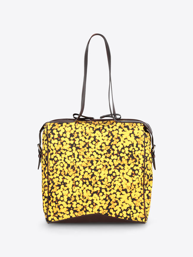A square-shaped shoulder bag with a bright yellow and black floral patterned body, featuring dark brown leather trim and a single shoulder strap, shown against a plain light gray background.