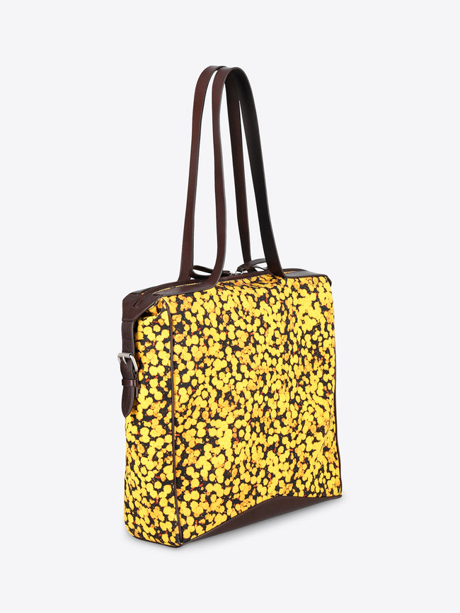 A square-shaped shoulder bag with a bright yellow and black floral patterned body, featuring dark brown leather trim and a single shoulder strap, shown against a plain light gray background.