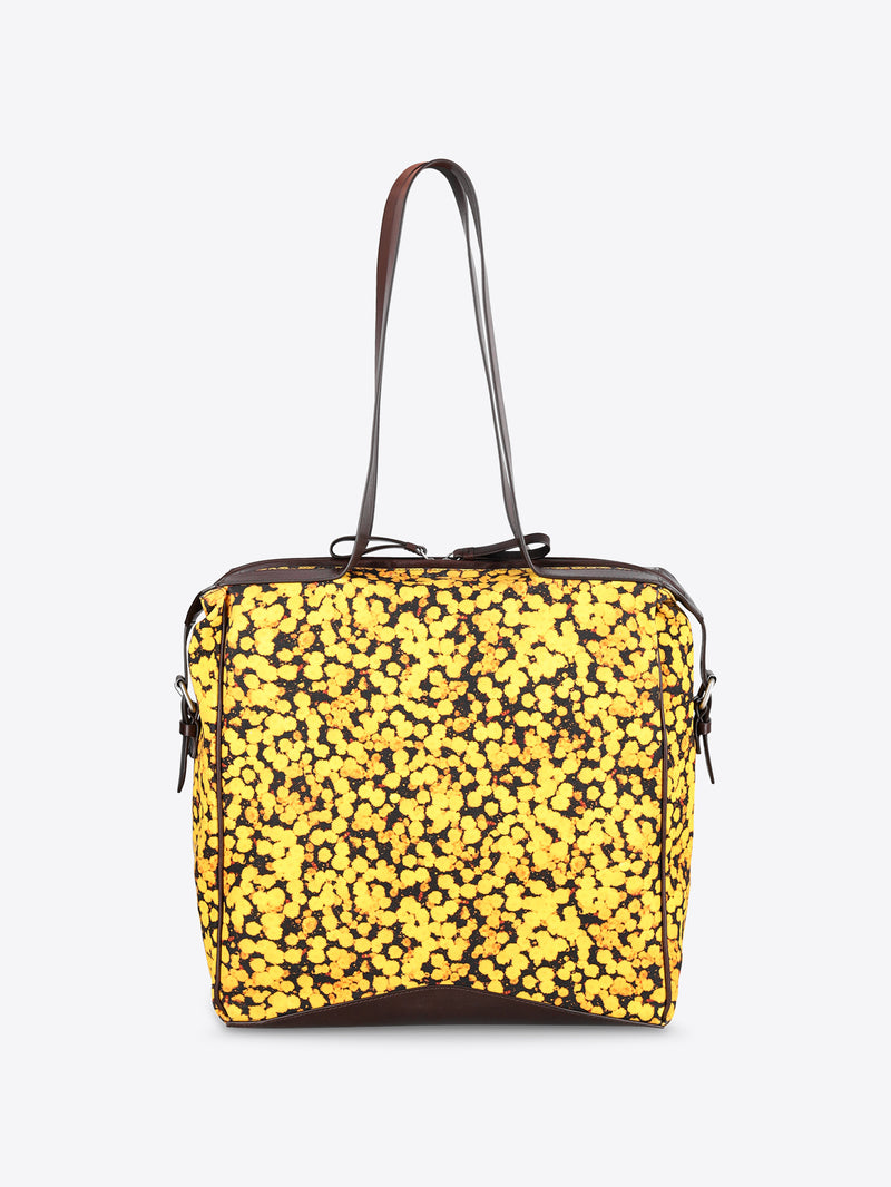 A square-shaped shoulder bag with a bright yellow and black floral patterned body, featuring dark brown leather trim and a single shoulder strap, shown against a plain light gray background.