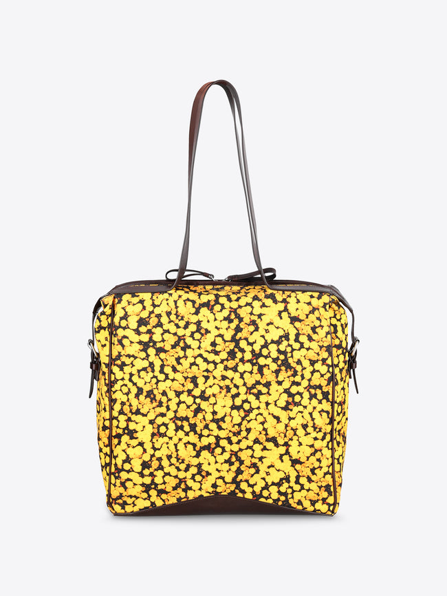 A square-shaped shoulder bag with a bright yellow and black floral patterned body, featuring dark brown leather trim and a single shoulder strap, shown against a plain light gray background.
