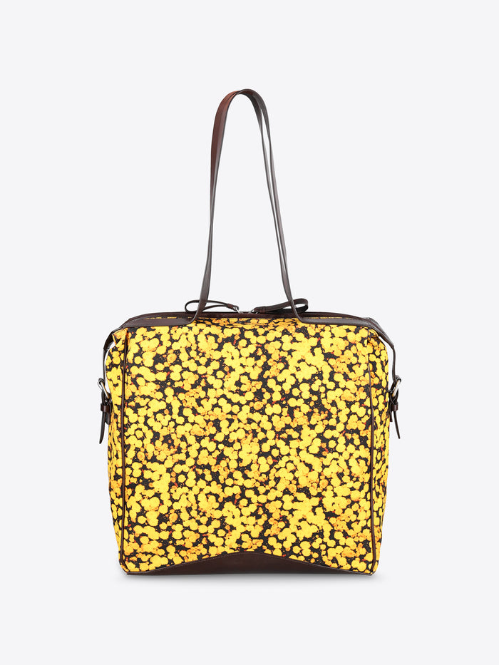 A square-shaped shoulder bag with a bright yellow and black floral patterned body, featuring dark brown leather trim and a single shoulder strap, shown against a plain light gray background.