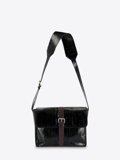 A black leather messenger bag with a brown leather strap detail and silver buckle, featuring a wide adjustable shoulder strap, shown against a light gray background.