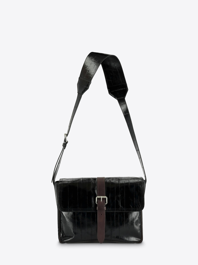 A black leather messenger bag with a brown leather strap detail and silver buckle, featuring a wide adjustable shoulder strap, shown against a light gray background.