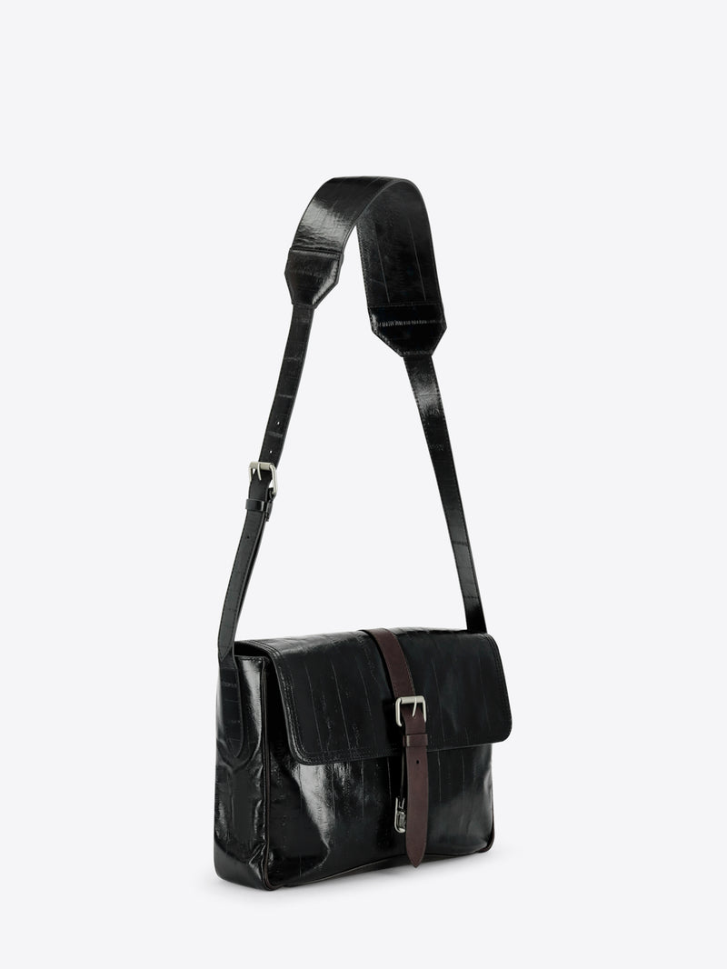 A black leather shoulder bag with a glossy finish, featuring a brown leather strap detail and silver buckle on the front flap, set against a light gray background.