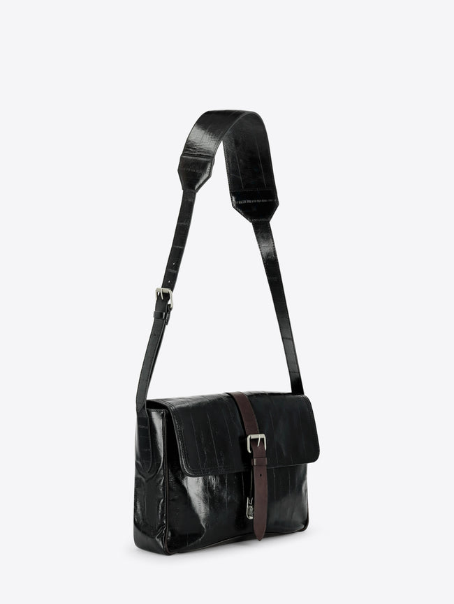 A black leather shoulder bag with a glossy finish, featuring a brown leather strap detail and silver buckle on the front flap, set against a light gray background.