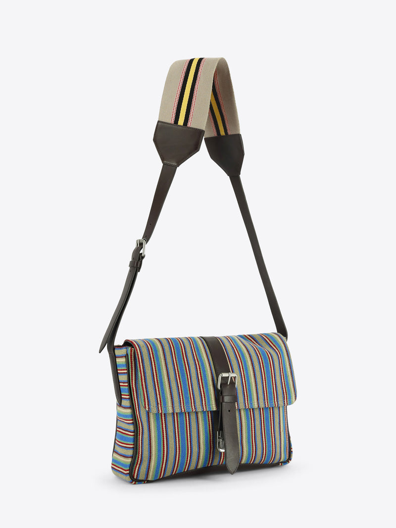 Multicolored striped shoulder bag with dark brown leather trim, a front buckle closure and an adjustable striped strap, shown against a light grey background.