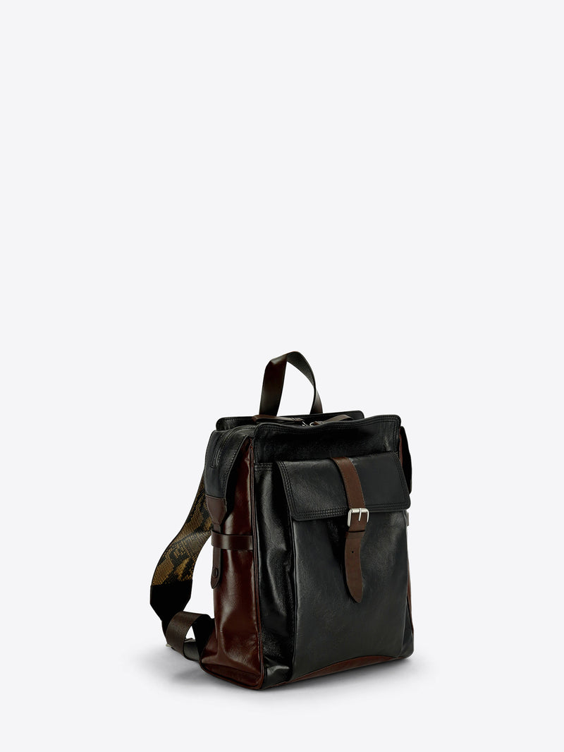 A dark brown and black leather backpack with a front flap pocket and brown leather strap details, shown against a light gray background.