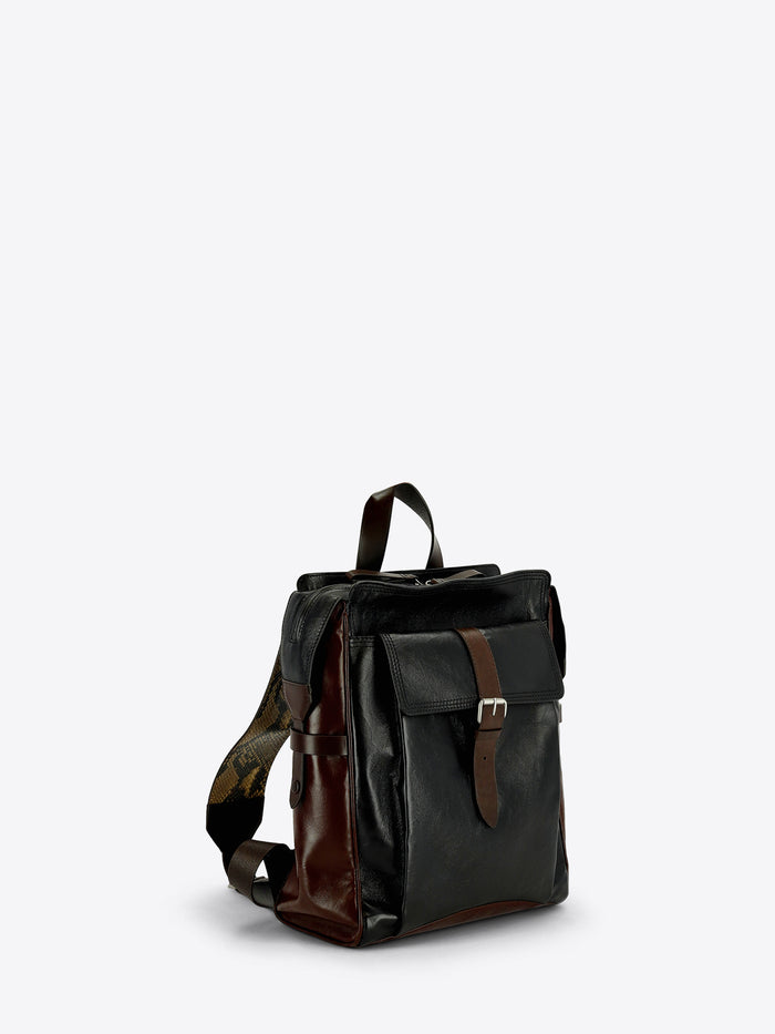 A dark brown and black leather backpack with a front flap pocket and brown leather strap details, shown against a light gray background.