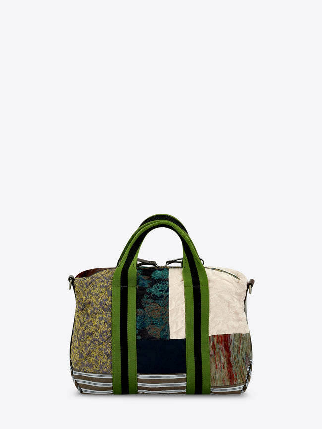 A patchwork tote bag featuring a mix of textures and prints, set against a light gray background.