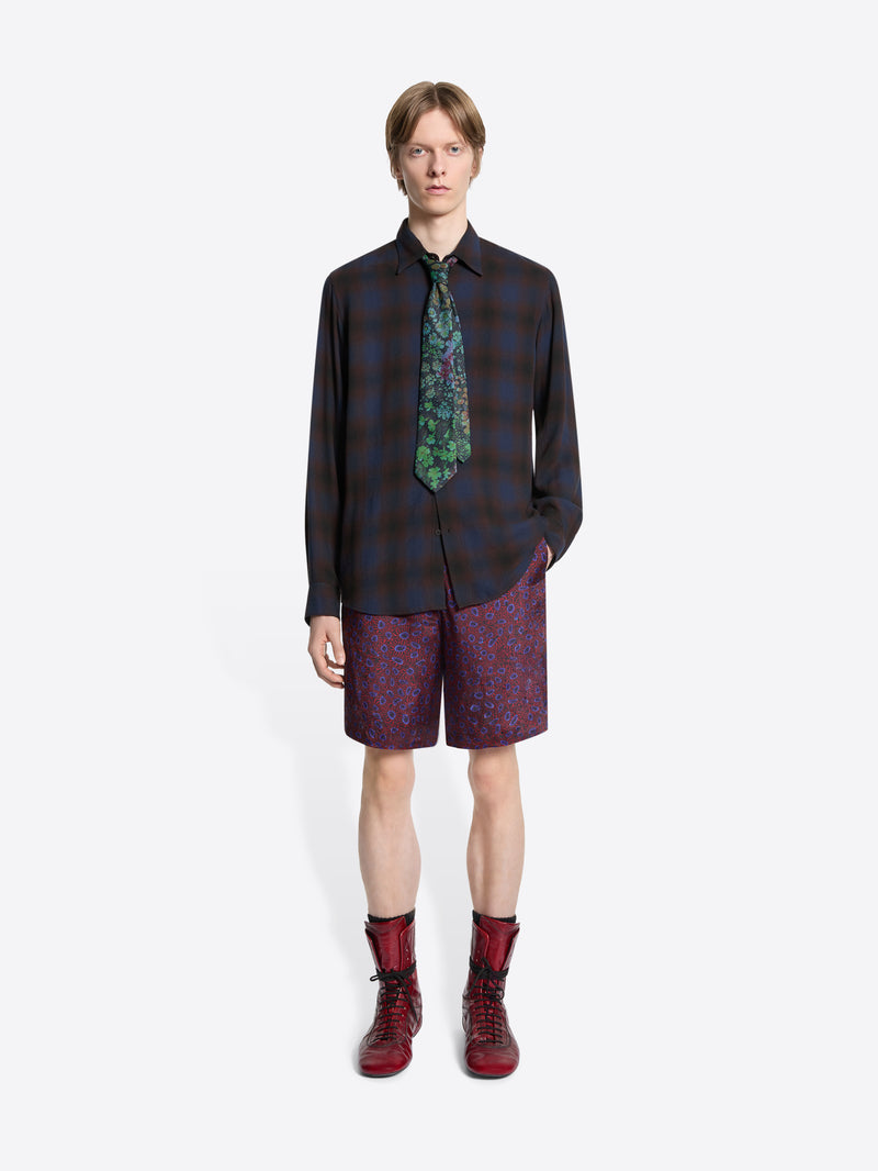 Person wearing a plaid shirt, patterned tie, purple shorts, and red boots on a white background