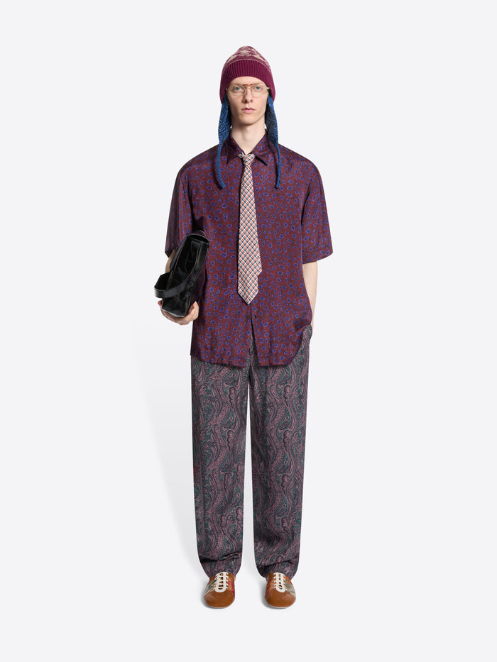 Person wearing a patterned shirt with a checkered tie, pants and hat on a white background