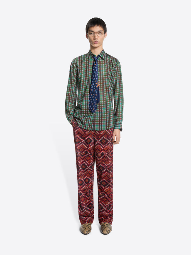 Person wearing a green plaid shirt with a dark tie and red patterned pants on a white background
