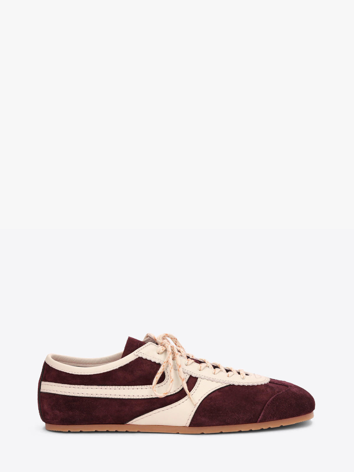 A low-top sneaker in burgundy suede and cream leather, featuring cream laces and a light tan rubber sole, shown on a light gray background. 