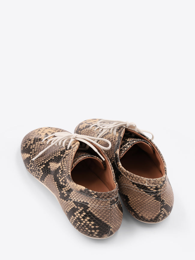 A pair of low-top lace-up shoes with a snakeskin pattern, featuring white laces, on a light gray background.