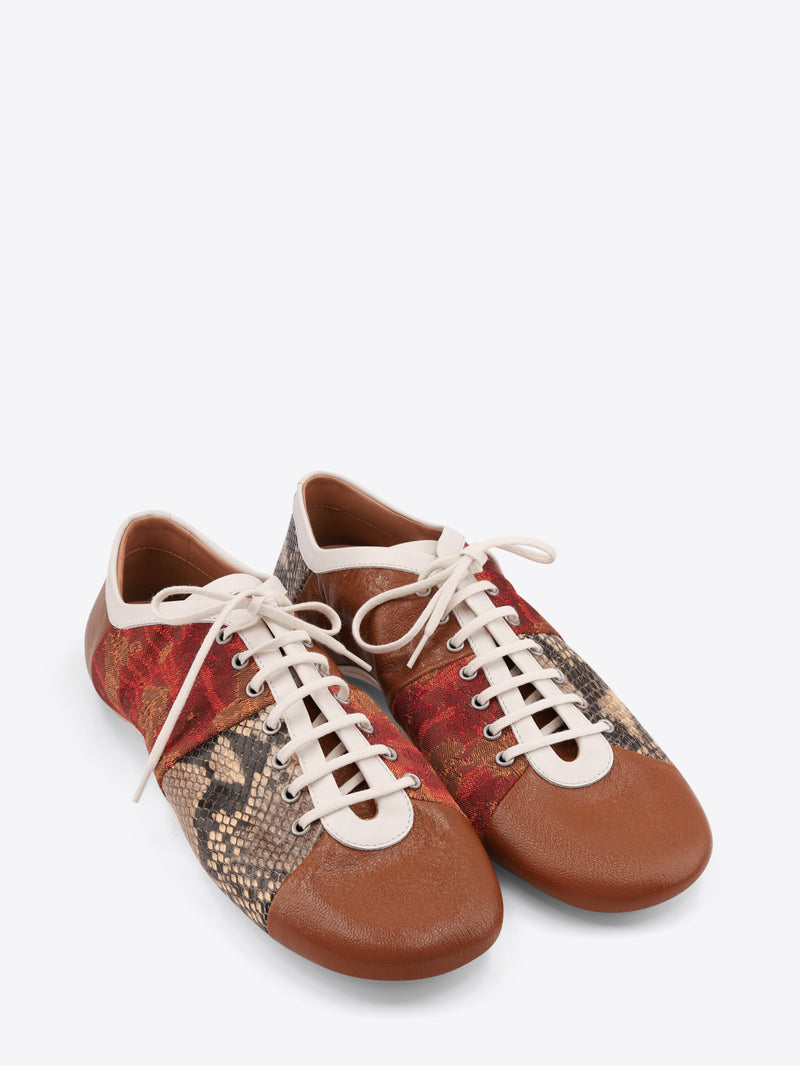 A pair of low-top lace-up shoes featuring a brown leather toe and heel, a red and gold patterned side panel, and a snakeskin-patterned panel on the front, set against a light gray background.