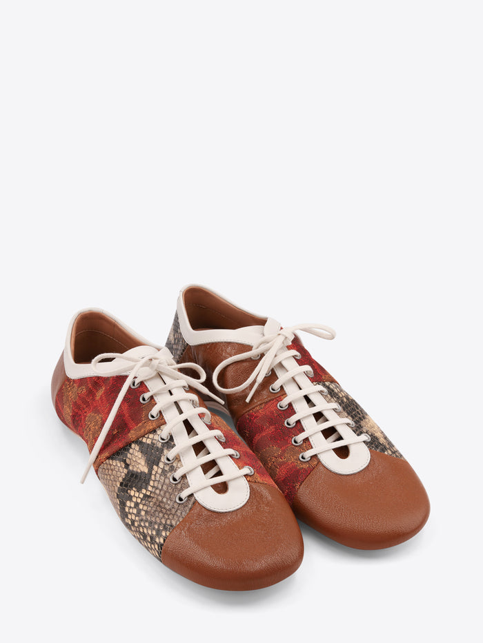 A pair of low-top lace-up shoes featuring a brown leather toe and heel, a red and gold patterned side panel, and a snakeskin-patterned panel on the front, set against a light gray background.