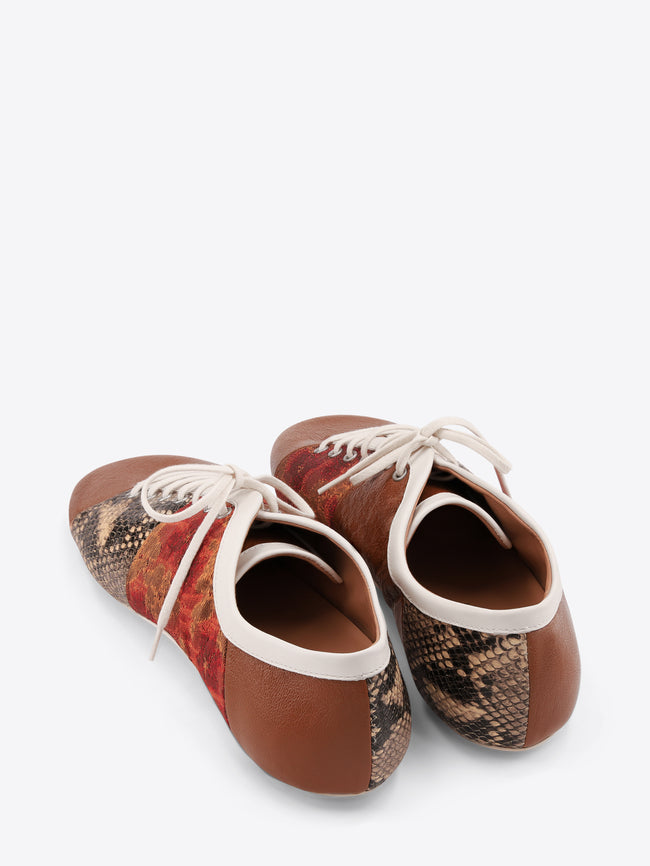 A pair of low-top lace-up shoes featuring a brown leather toe and heel, a red and gold patterned side panel, and a snakeskin-patterned panel on the front, set against a light gray background.