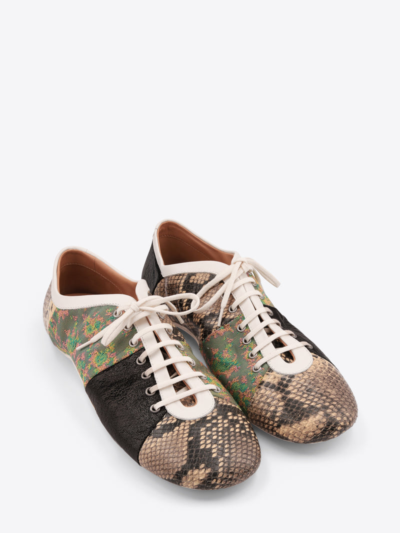 A pair of low-top sneakers featuring mixed animal print panels, including a beige snakeskin pattern, a green and brown floral section, a black textured panel, and a beige snakeskin pattern on the toe with white laces on a light gray background.
