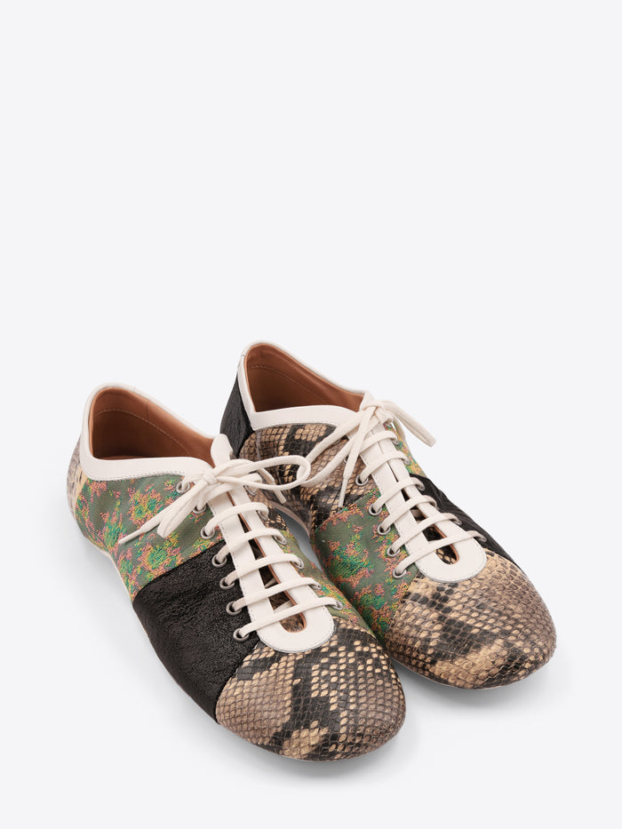 A pair of low-top sneakers featuring mixed animal print panels, including a beige snakeskin pattern, a green and brown floral section, a black textured panel, and a beige snakeskin pattern on the toe with white laces on a light gray background.