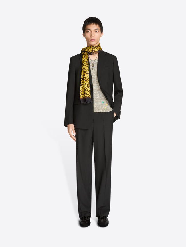 Person wearing a black suit with a yellow patterned scarf on a light gray background