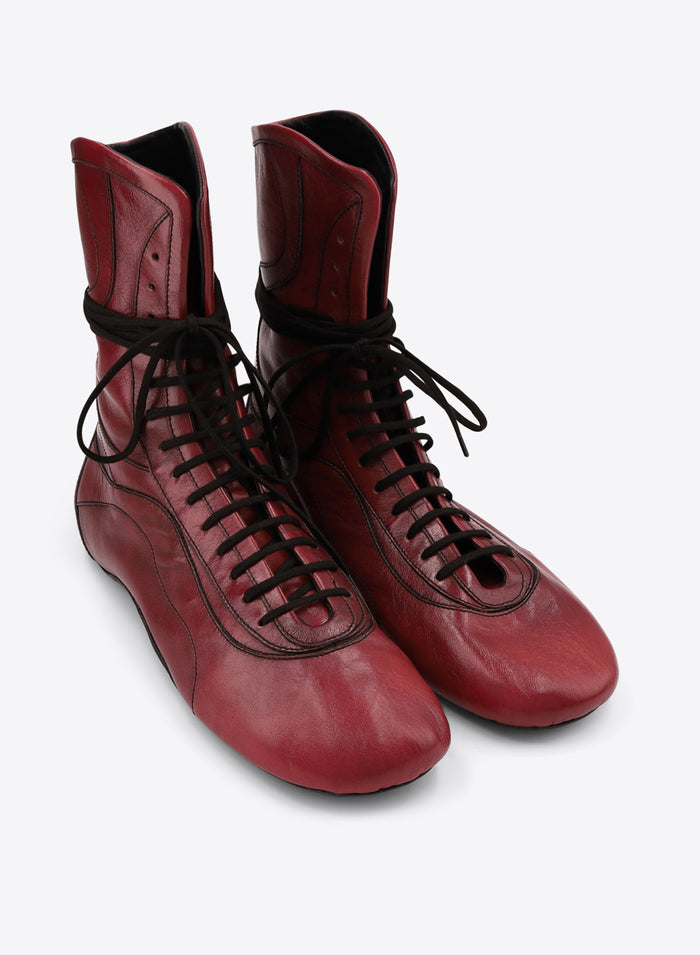 A pair of red leather lace-up boots with black laces, shown on a light gray background.