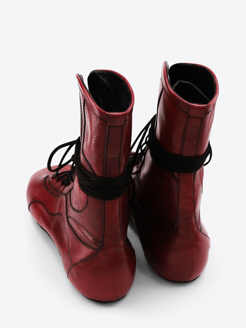A pair of red leather lace-up boots with black laces, shown on a light gray background.