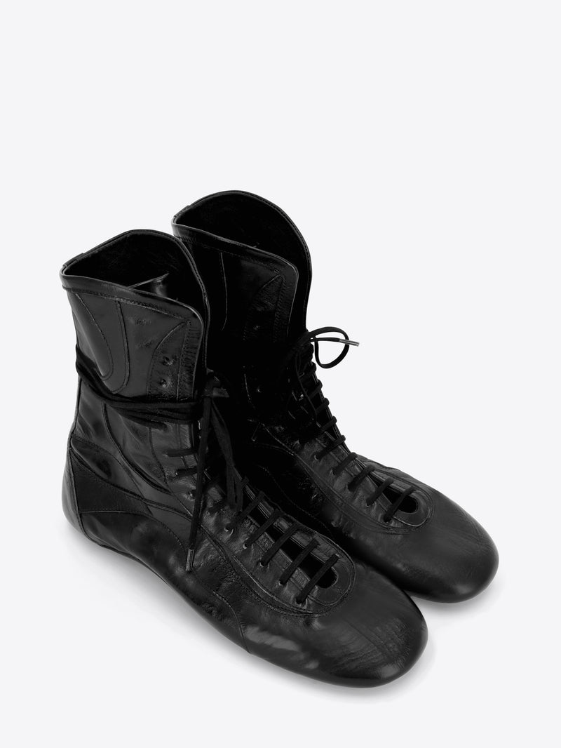 A pair of black leather lace-up high-top shoes with a glossy finish, shown on a light gray background.