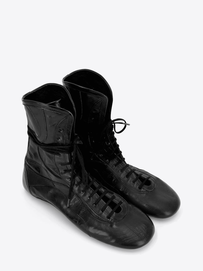 A pair of black leather lace-up high-top shoes with a glossy finish, shown on a light gray background.
