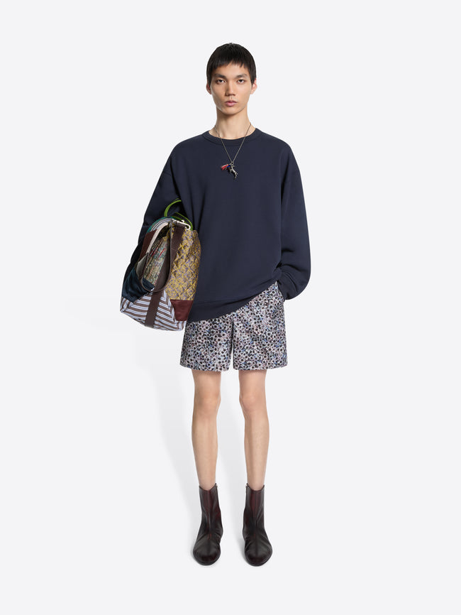 Person wearing a navy sweatshirt, patterned shorts, and dark boots on a light gray background