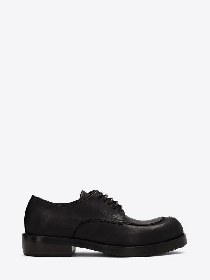 Black leather lace-up shoe with an apron toe, chunky sole, and low stacked heel on a light gray background.