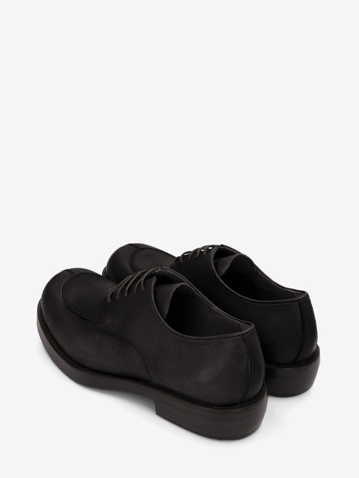 A pair of black leather lace-up shoes with an apron toe, chunky sole, and low stacked heel on a light gray background.
