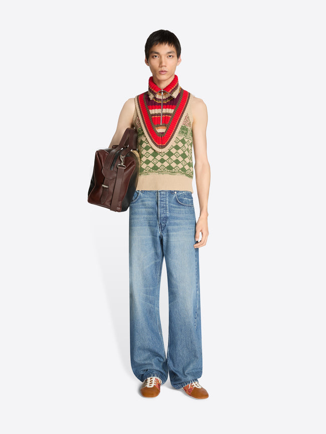 Person wearing a patterned vest, striped knitted detached collar and blue jeans with a brown bag on a white background