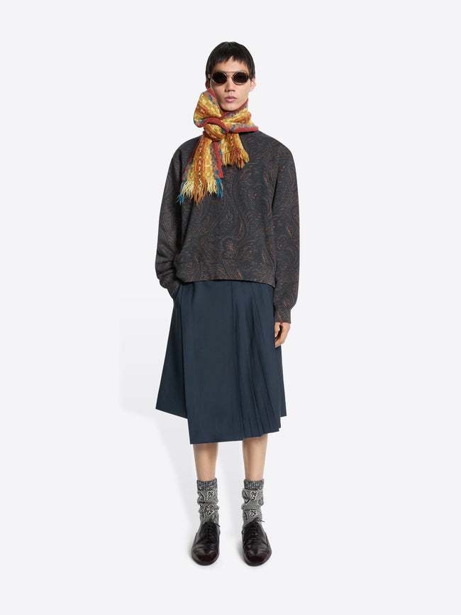 Person wearing a patterned sweatshirt, dark skirt, and colorful scarf on a white background