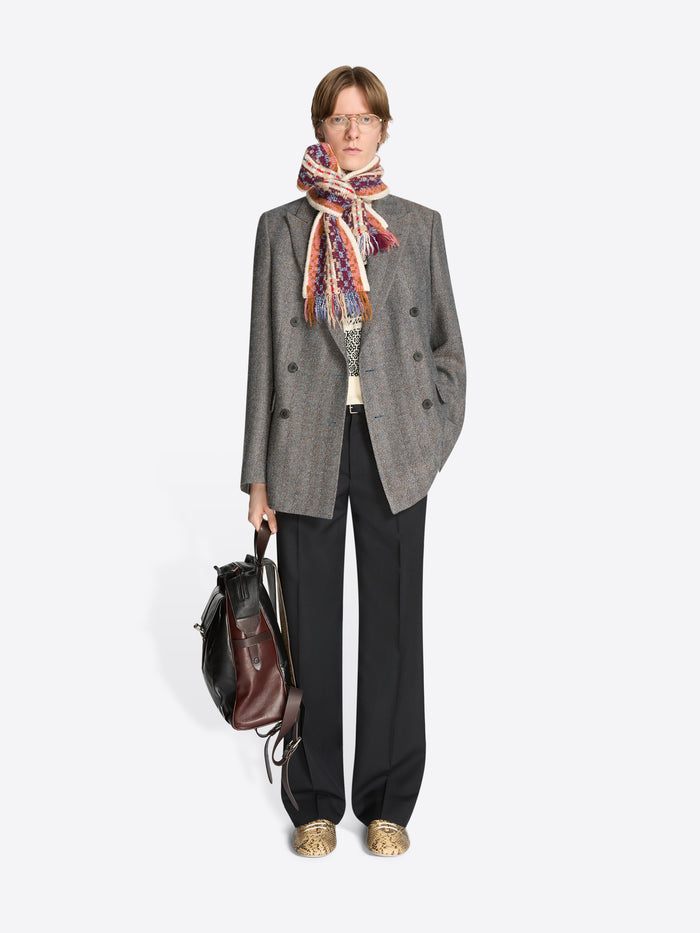 Person wearing a gray coat with a colorful scarf, holding a backpack on a white background