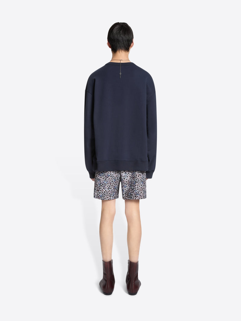 Person wearing a navy sweatshirt and patterned swim shorts on a white background
