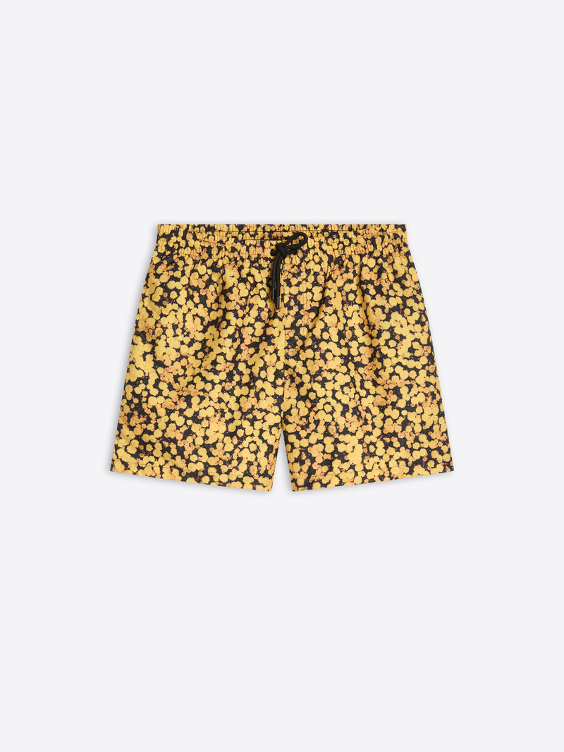 A pair of men's swim trunks featuring a dense yellow and black abstract floral, with a black drawstring at the elastic waistband, shown flat on a light gray background.