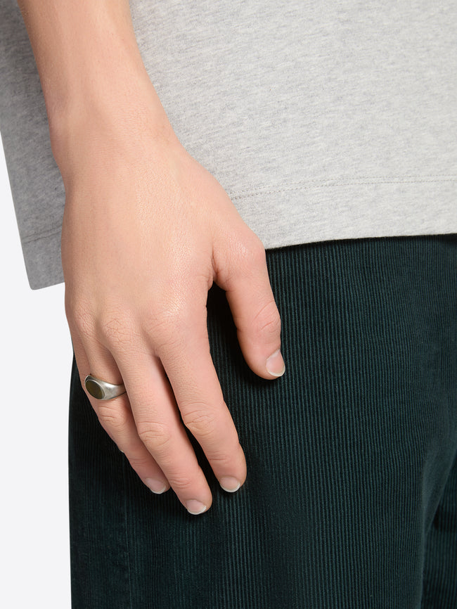 A close-up of a person's hand resting on dark green corduroy trousers, wearing a silver-toned signet ring. 