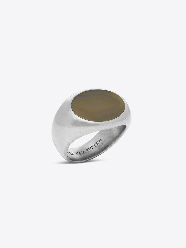 A silver signet ring with a polished oval face, featuring the engraved brand name 'DRIES VAN NOTEN' inside the band, set against a light gray background.