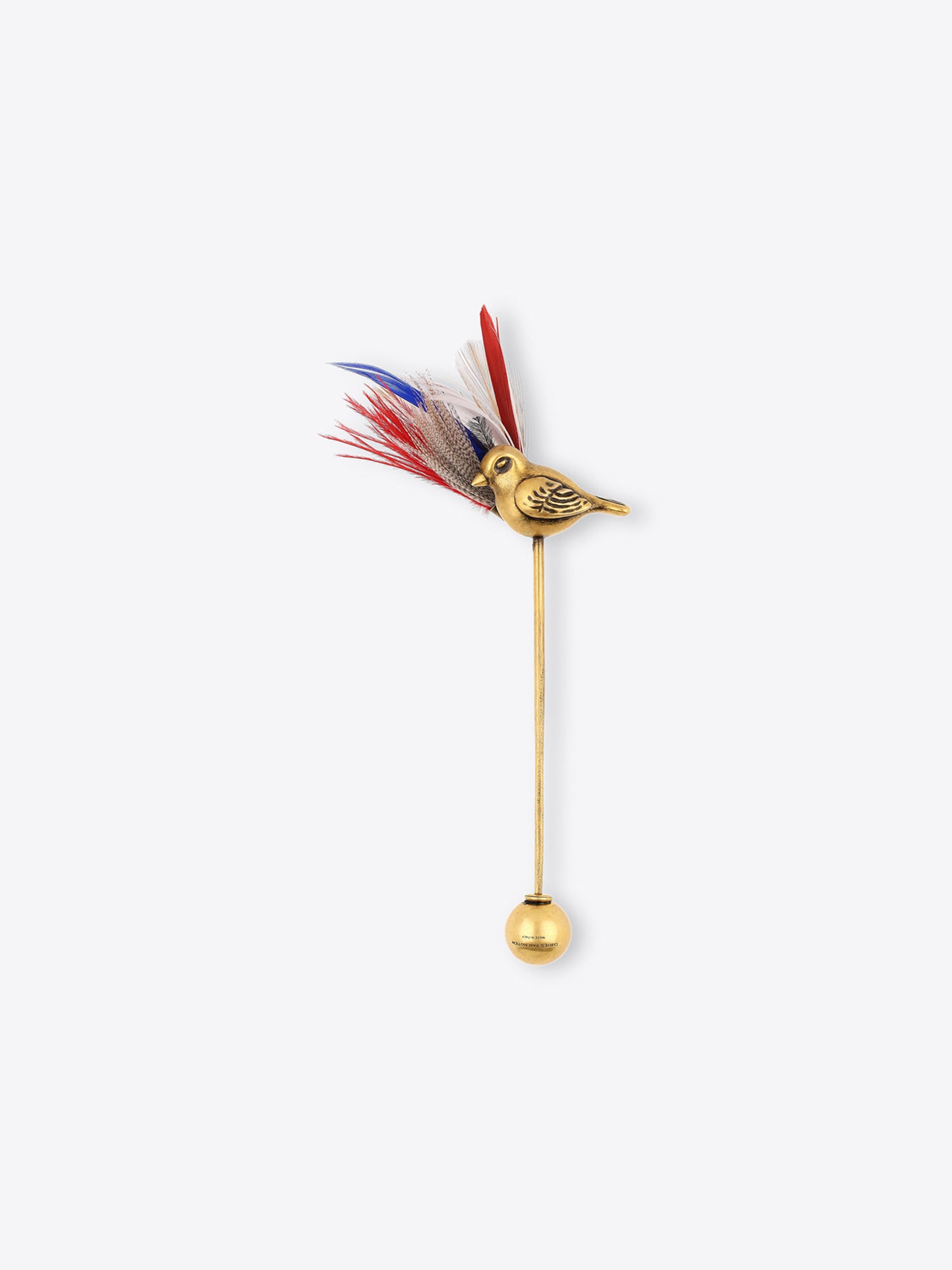 A gold-tone bird-shaped brooch with a long stem and a round ball at the bottom, topped with red, white, and blue feathers, shown on a light gray background.