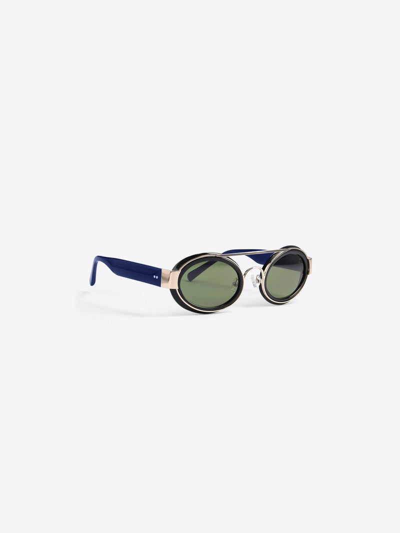 A round black-rimmed sunglasses with dark green lenses, a double-layered black and gold metal frame, and navy blue temples, shown on a light gray background.