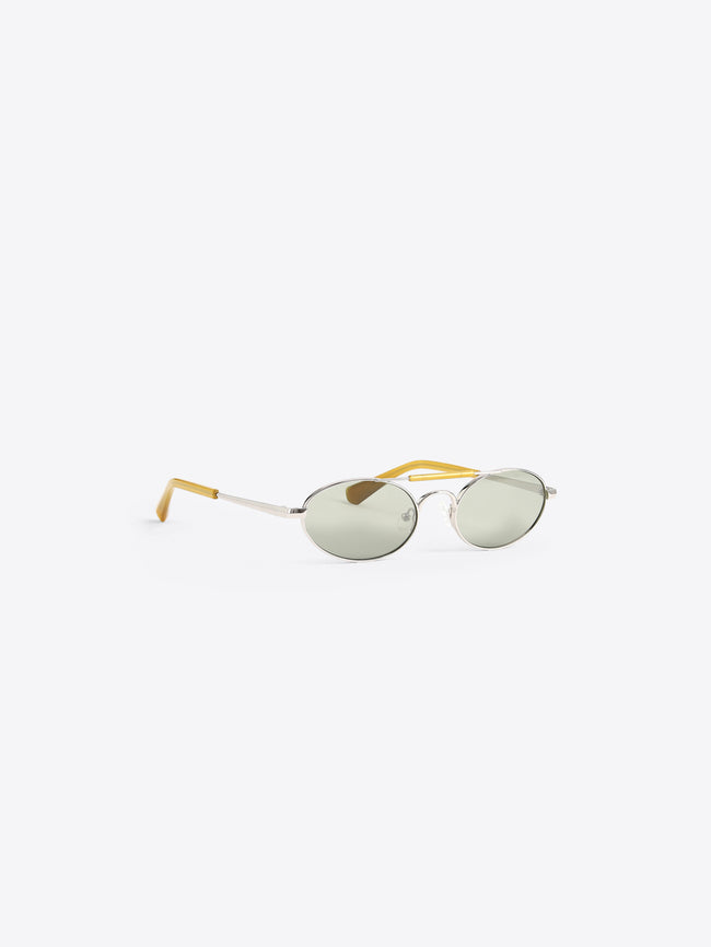Oval sunglasses with light green tinted lenses, a silver metal frame, and yellow acetate temples, shown on a light gray background.