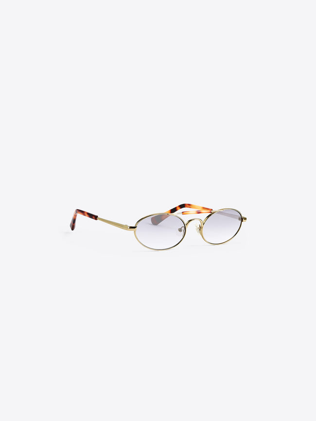 Oval eyeglasses with a gold metal frame, clear-to-light-tinted lenses, and tortoiseshell-patterned temples, shown on a light gray background.