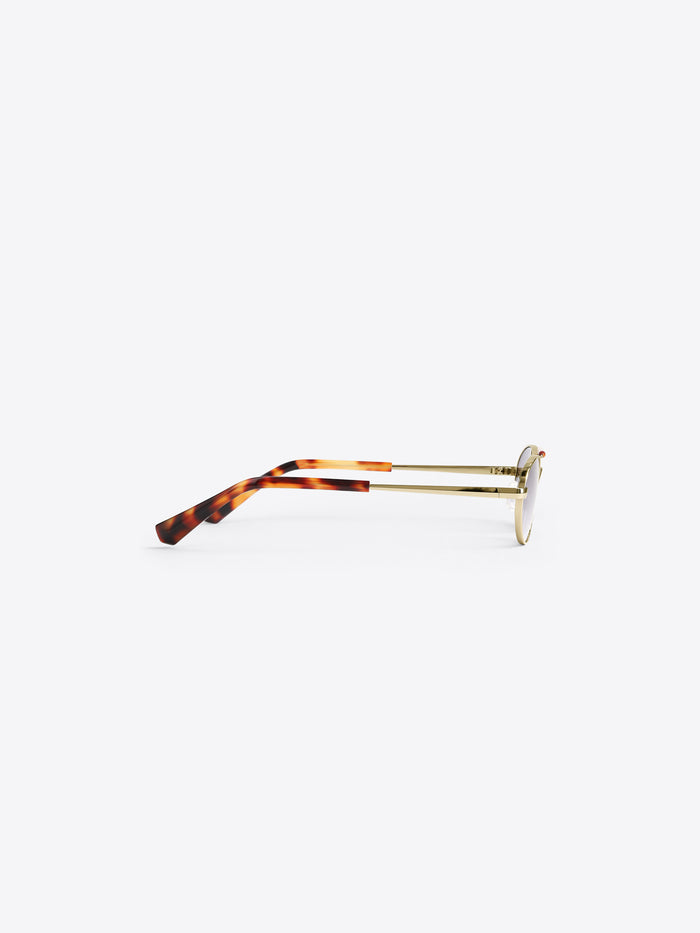 Oval eyeglasses with a tortoiseshell acetate frame and gold metal temples, shown from a side profile on a light gray background. 