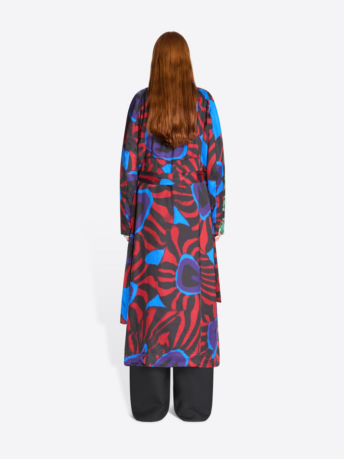 Back view of a long abstract-print coat in red, blue and black tones, worn with black trousers 